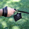 Hand holding leash with Tre Ponti Bag Dispenser in Black against grassy background